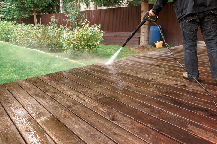 Man cleaning walls and floor with high pressure power washer. Washing terrace wood planks and cladding walls.